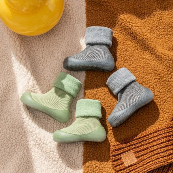 Green and gray ribbed sock shoes with soft folded cuffs on a textured blanket.