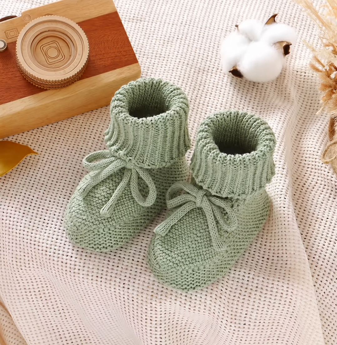 Green knitted baby booties with folded ribbed cuffs and matching ties