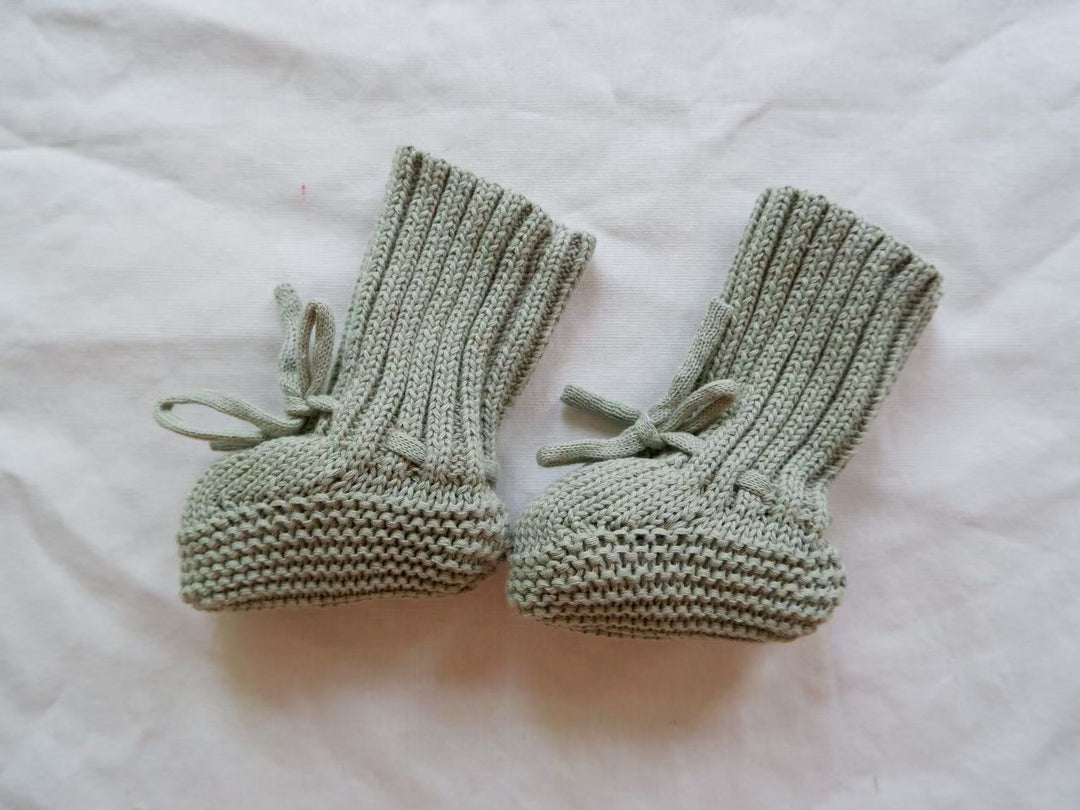 Green knitted baby booties with tall ribbed cuffs and matching ties.