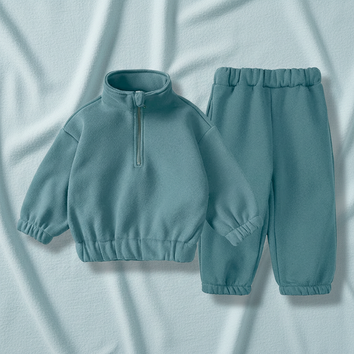 Green quarter-zip sweatshirt and matching joggers arranged on pale blue fabric