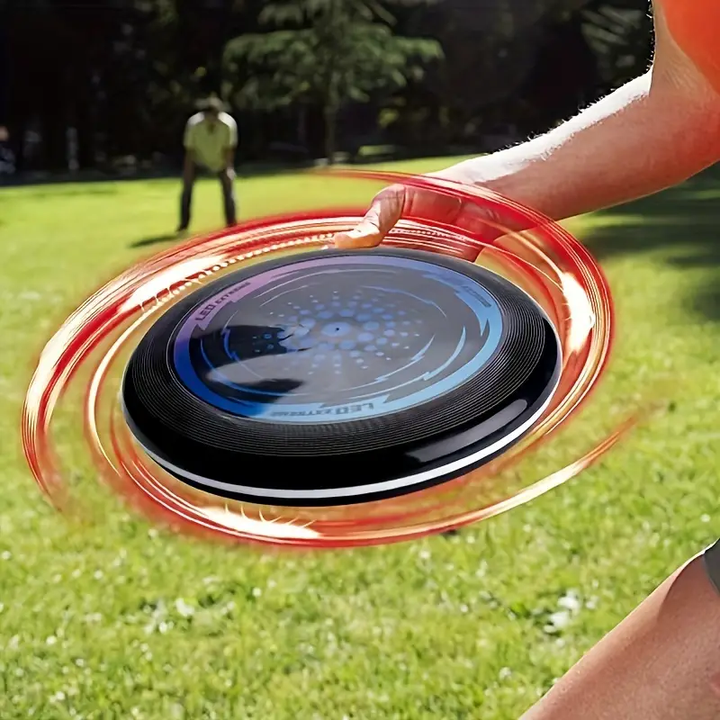Hand holding a flying disc with an illuminated rim during an outdoor game