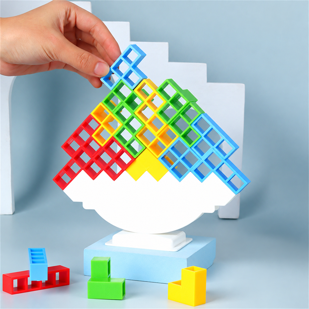 A hand places a blue block on a tower balanced on a curved white platform.