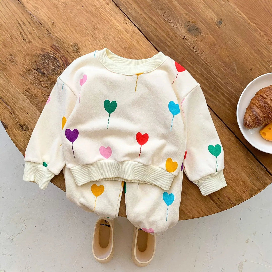 Heart-print baby tracksuit with a crewneck sweater and cuffed pants on a wooden table