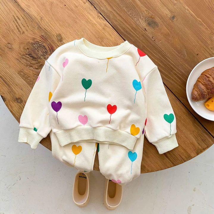 Heart-print baby tracksuit with a crewneck sweater and cuffed pants on a wooden table