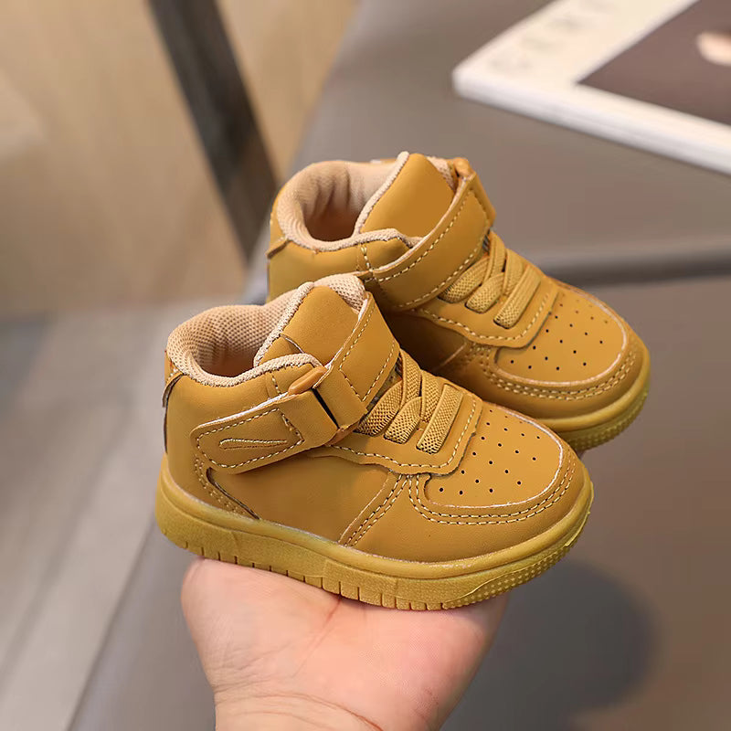 Khaki high-top sneakers held in a hand, showing straps and perforated toes