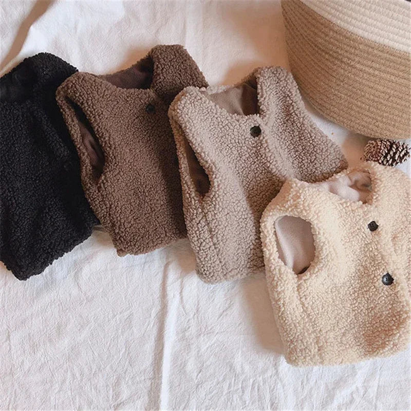 Black, brown, beige, and white kids' plush vests arranged in a row