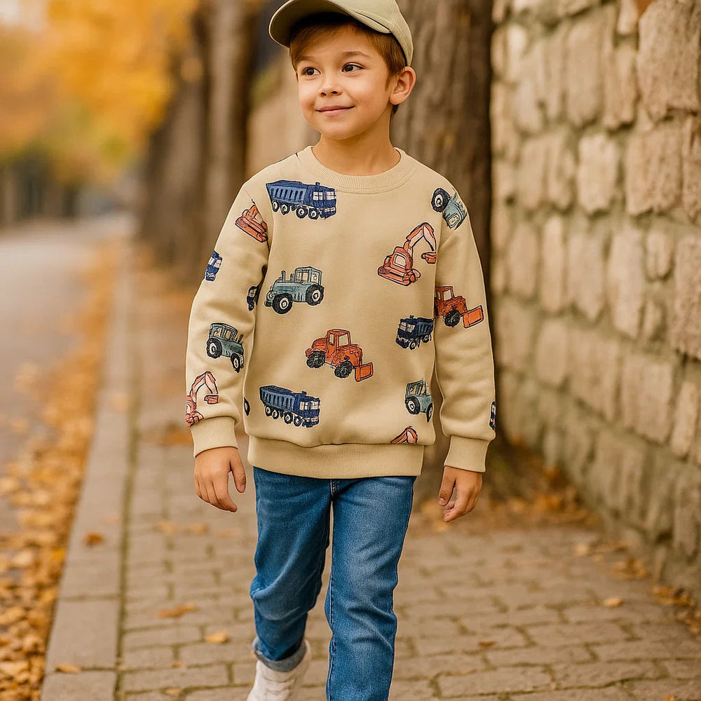 Child wearing a beige construction vehicle sweatshirt with jeans on a fall sidewalk