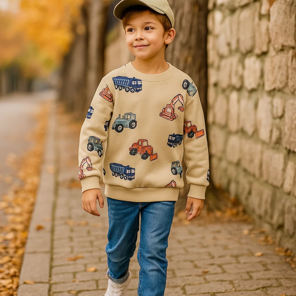 Child wearing a beige construction vehicle sweatshirt with jeans on a fall sidewalk