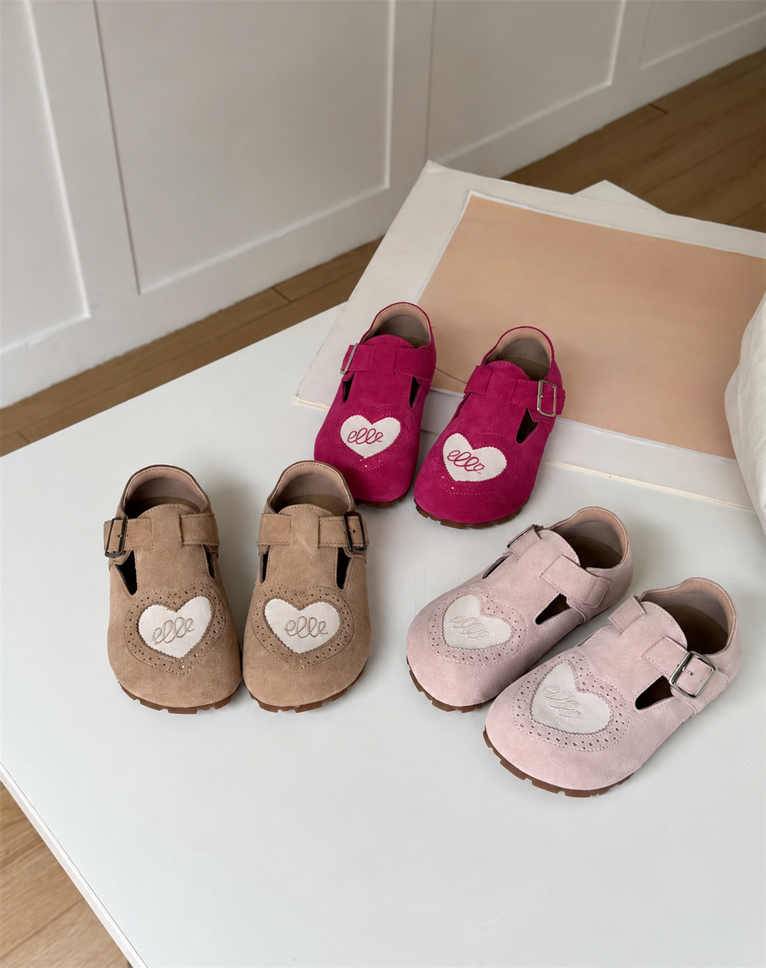 Three pairs of leather heart-detail shoes in brown, pink, and red on a white bench