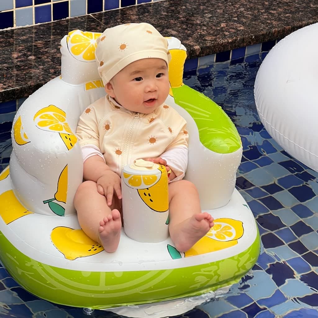 Baby sitting in a lemon-print inflatable baby seat with a green base and rounded armrests.
