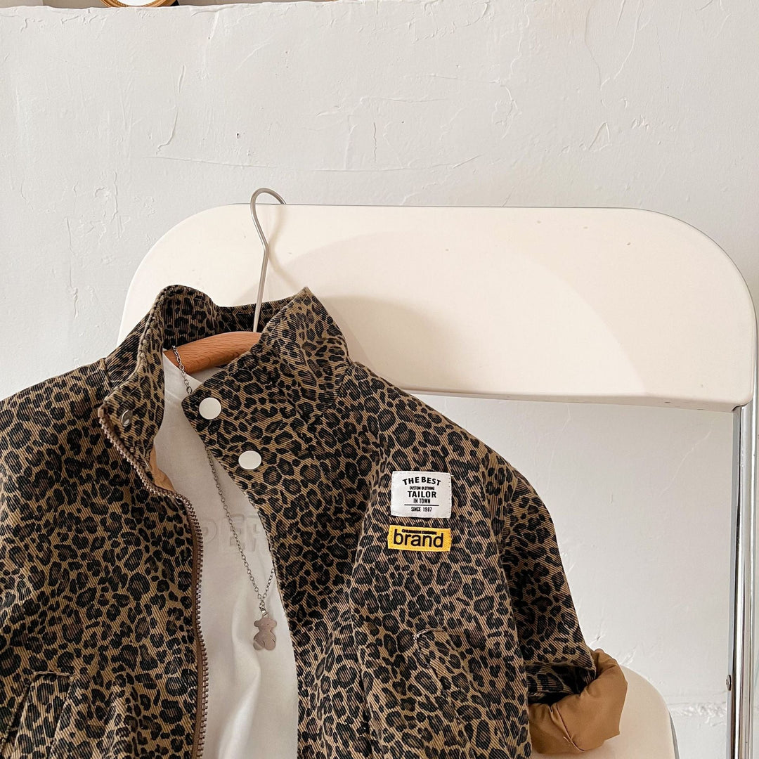 Front of a leopard print jacket on a chair, showing its stand collar and chest patches