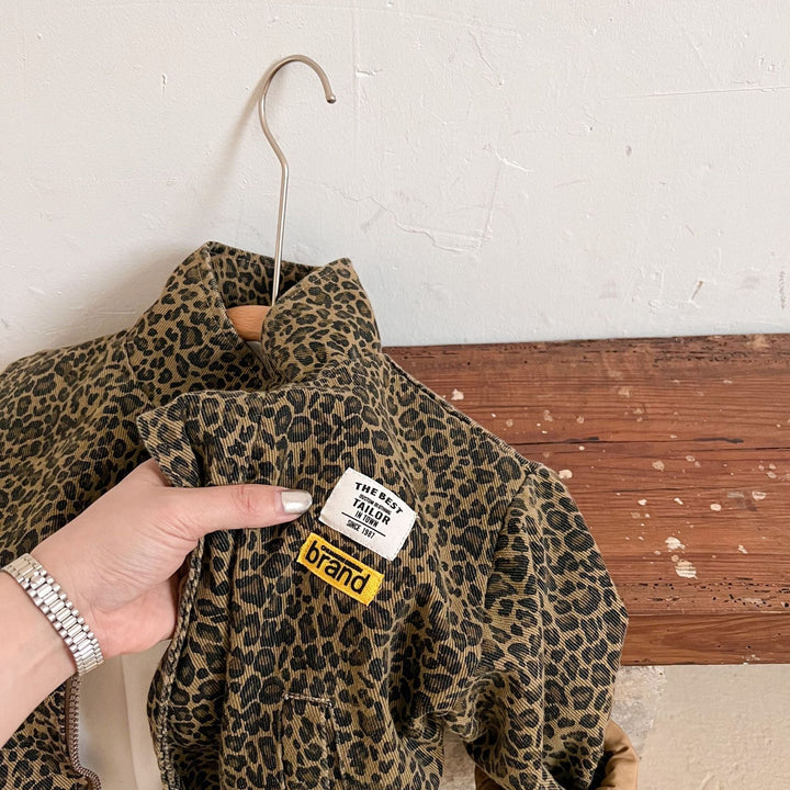 Hand holding the front of a leopard print jacket near the collar and chest patches