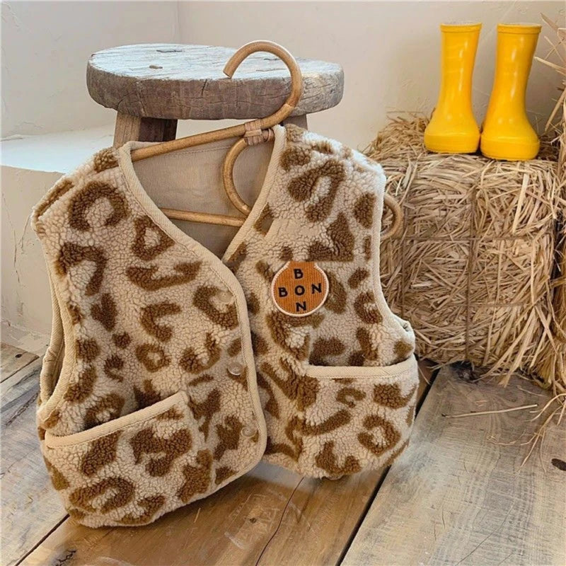 Leopard-print kids' vest with beige trim and two front pockets displayed beside yellow rain boots