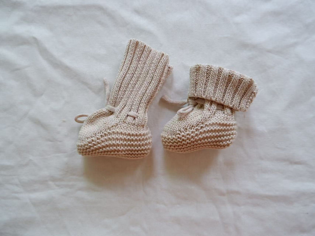 Light gray knitted baby booties showing an upright cuff and a folded cuff.