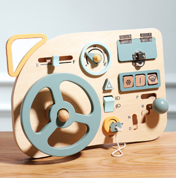 Wooden driving activity board with a green steering wheel, gear lever, slider, dial, and latched panel