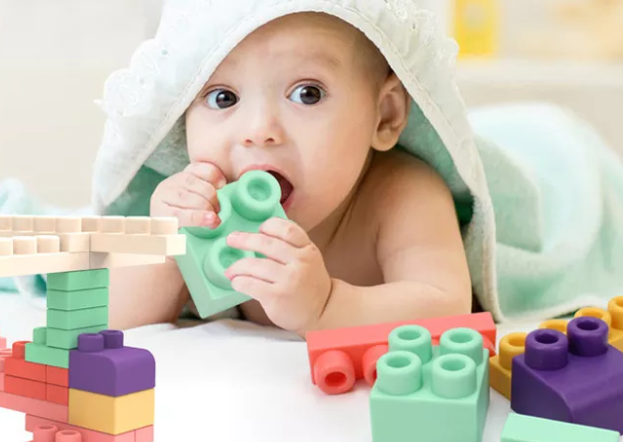 Baby holding a mint-green silicone block to the mouth beside block constructions