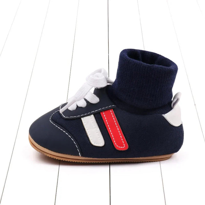 Side view of a navy baby shoe with a knit cuff, white laces, and red and white stripes