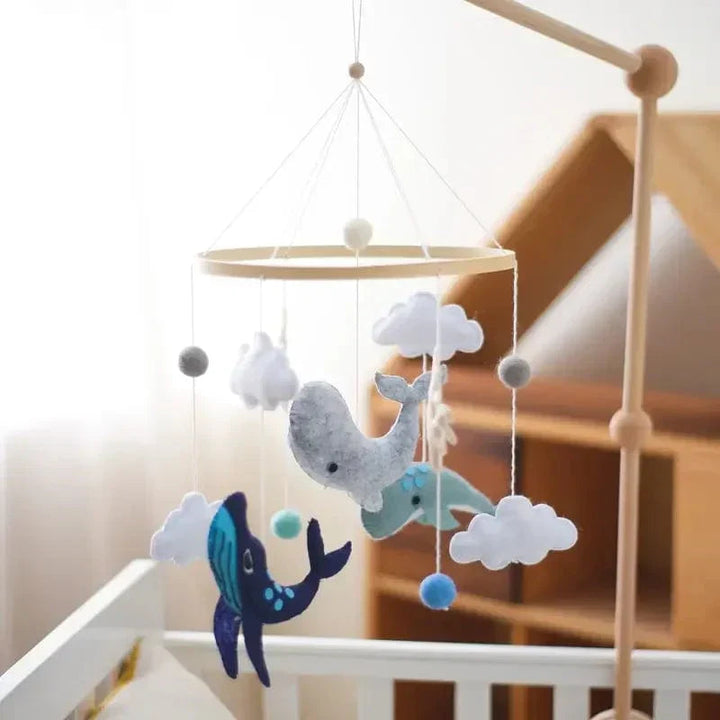 Ocean baby mobile with whales and clouds suspended from a wooden mounting arm beside a crib