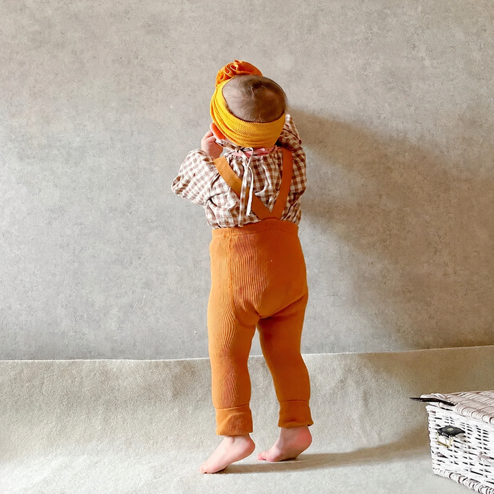 Baby wearing orange suspender leggings with a checked top