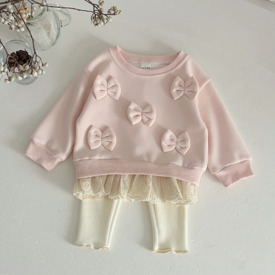 Pink bow sweater with lace trim and cream pants arranged on a light surface