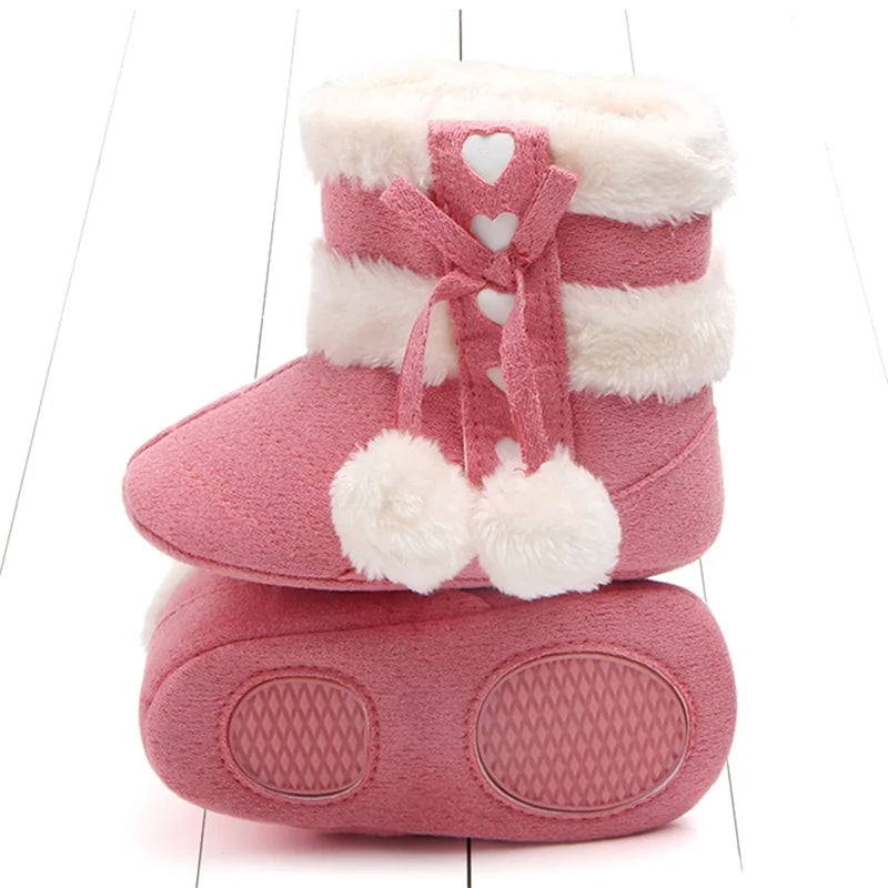 Pink baby snow boots showing fluffy trim, heart details, pom-poms, and the patterned sole