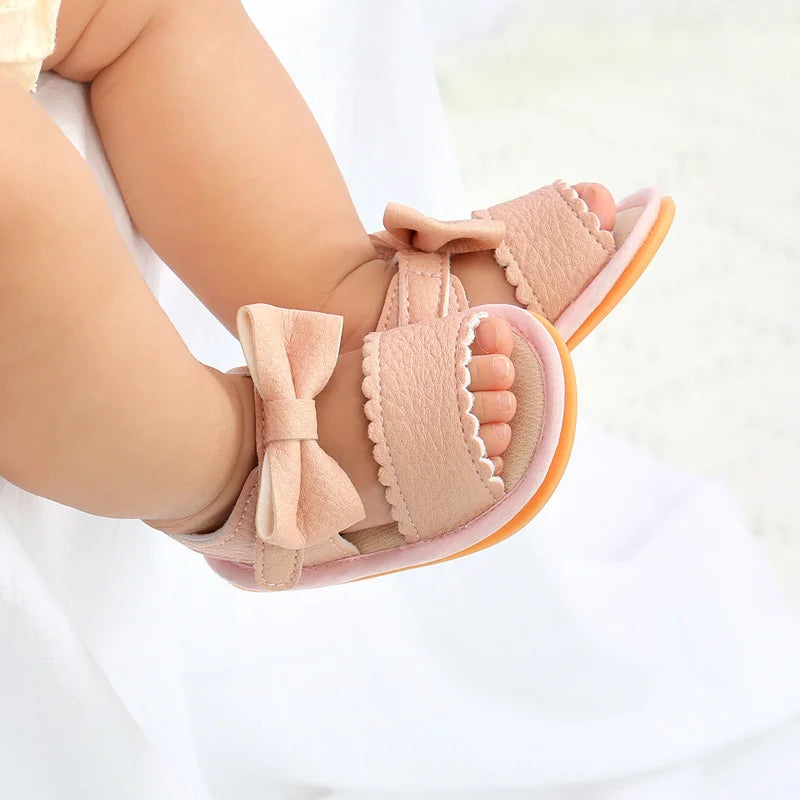 Close-up of a baby wearing pink open-toe sandals with bows and scalloped straps