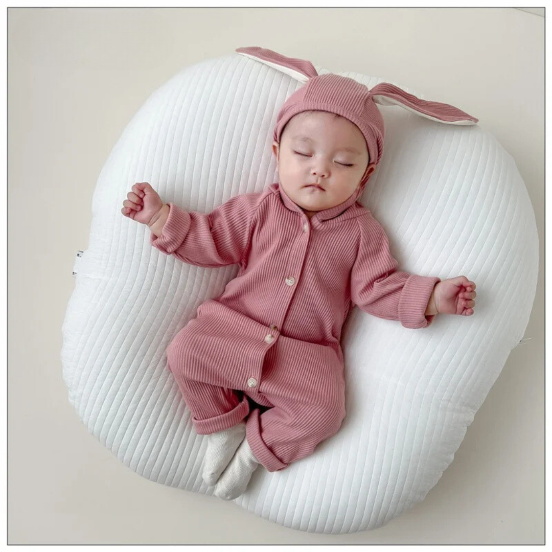 Baby wearing a pink bunny-ear romper while resting on a white cushion