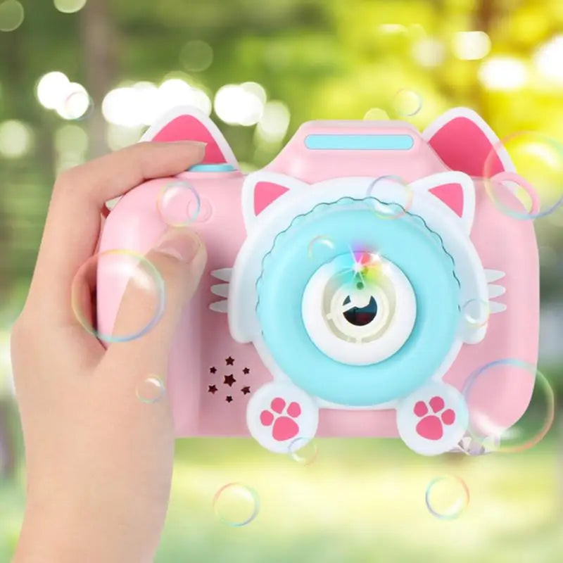 Pink cat-shaped bubble camera with a blue front, held outdoors among bubbles.