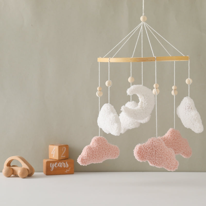 Pink and white cloud mobile displayed against a muted green nursery wall