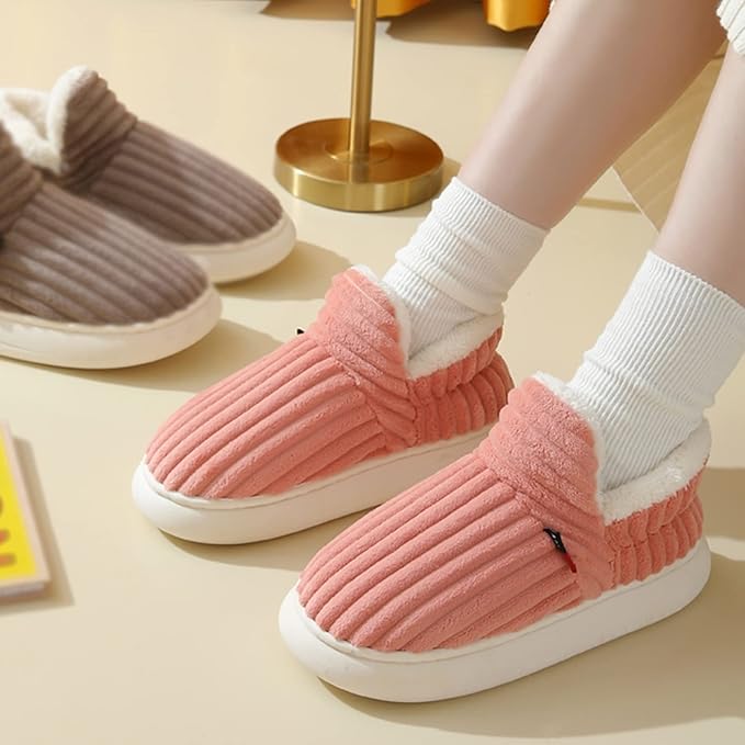 Pink corduroy slippers with white plush lining worn with white socks indoors.
