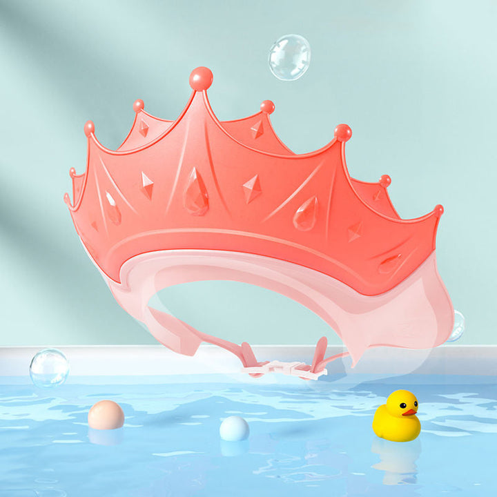 Pink crown-shaped bath visor with an adjustable band against a bubble-themed background