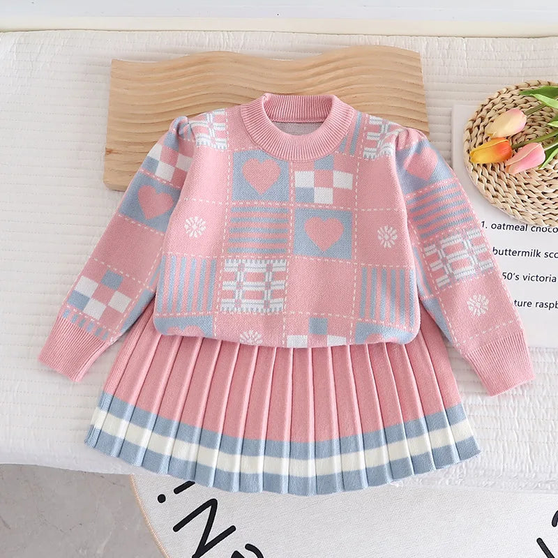 Pink knit sweater with blue heart and check patterns and a pleated skirt with a blue-and-white striped hem