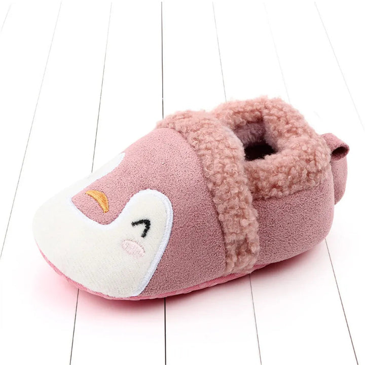 Pink penguin baby slipper with a white face, yellow beak, and fuzzy trim.
