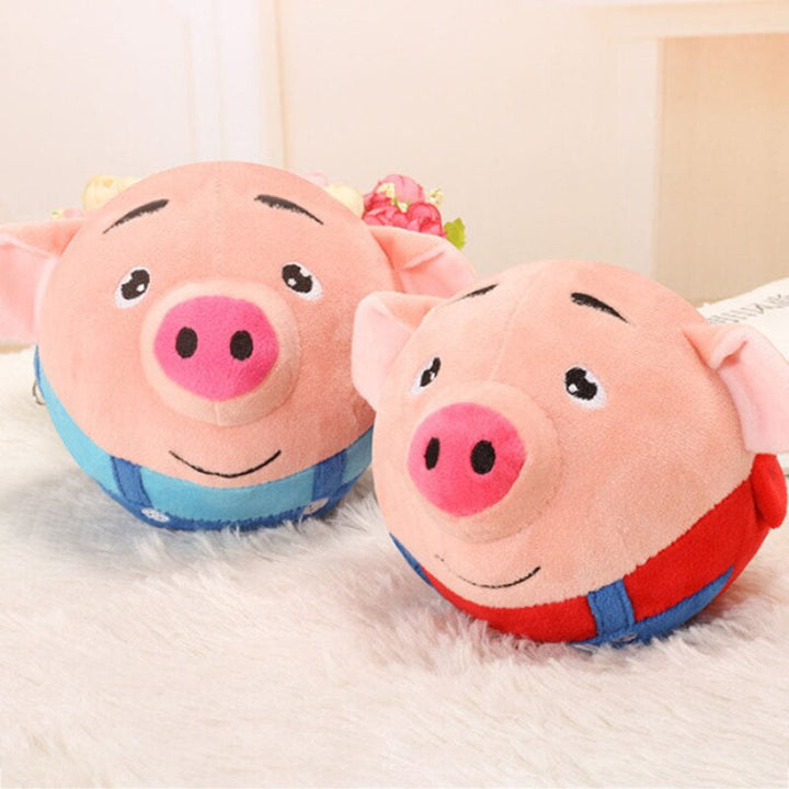Pink pig toy balls with blue and red outfits resting on a fluffy surface