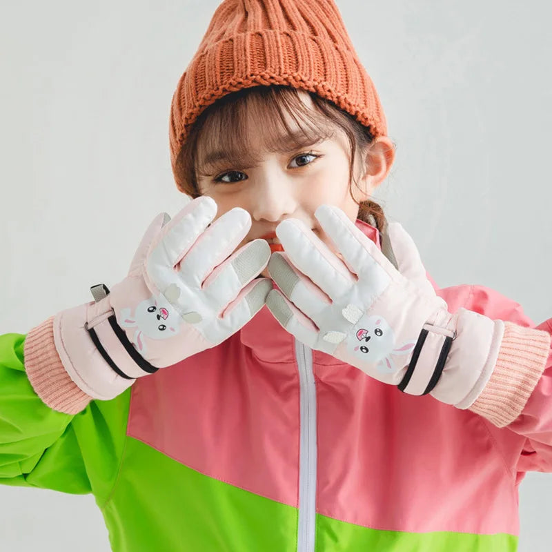 Child wearing pink rabbit ski gloves with an orange knit hat and a pink-and-green jacket.