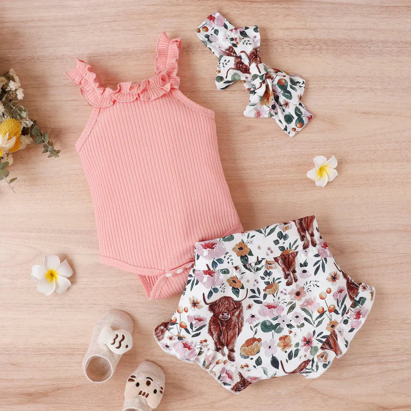 Pink ruffle-trim romper with printed shorts and a coordinating bow headband on a wood surface