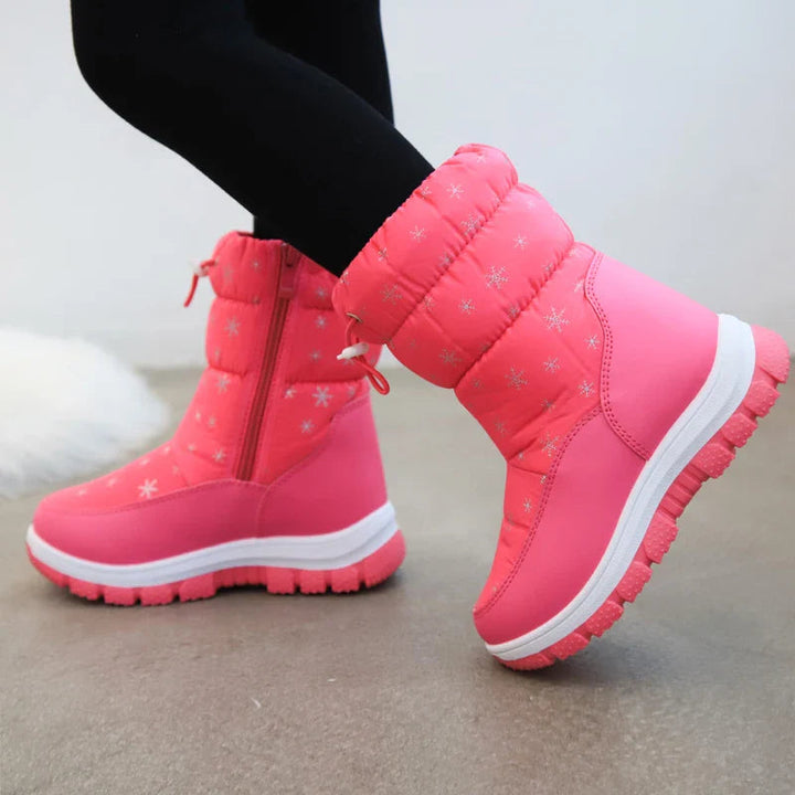 Pink snowflake-print snow boots worn with black leggings, showing side zippers and treaded soles
