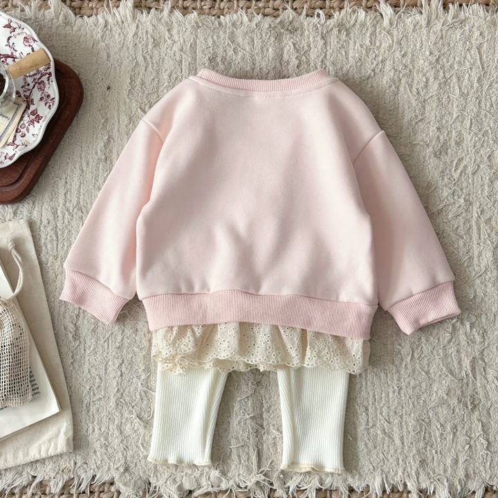 Back view of the pink baby sweater with lace trim above cream ribbed pants