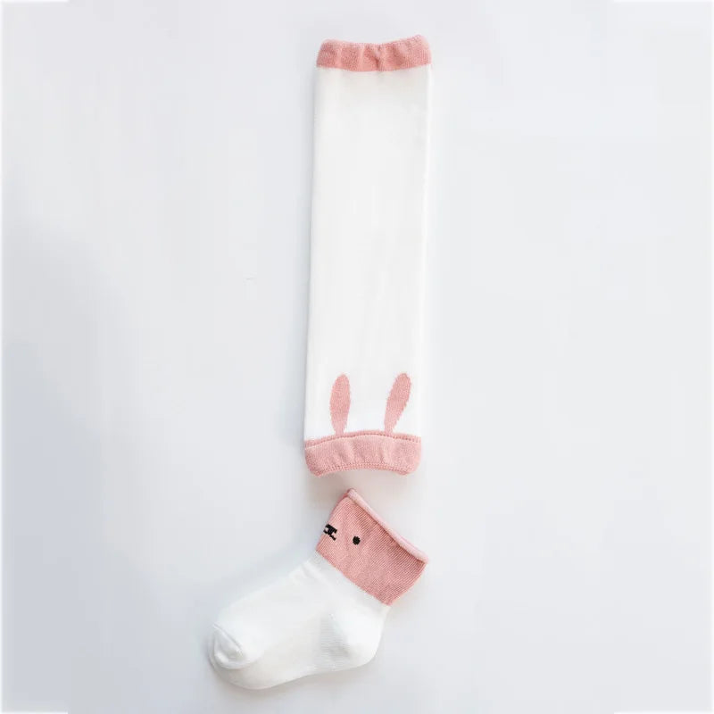 White baby leg warmer with pink trim and bunny-ear details beside a white sock with a pink animal-face cuff.