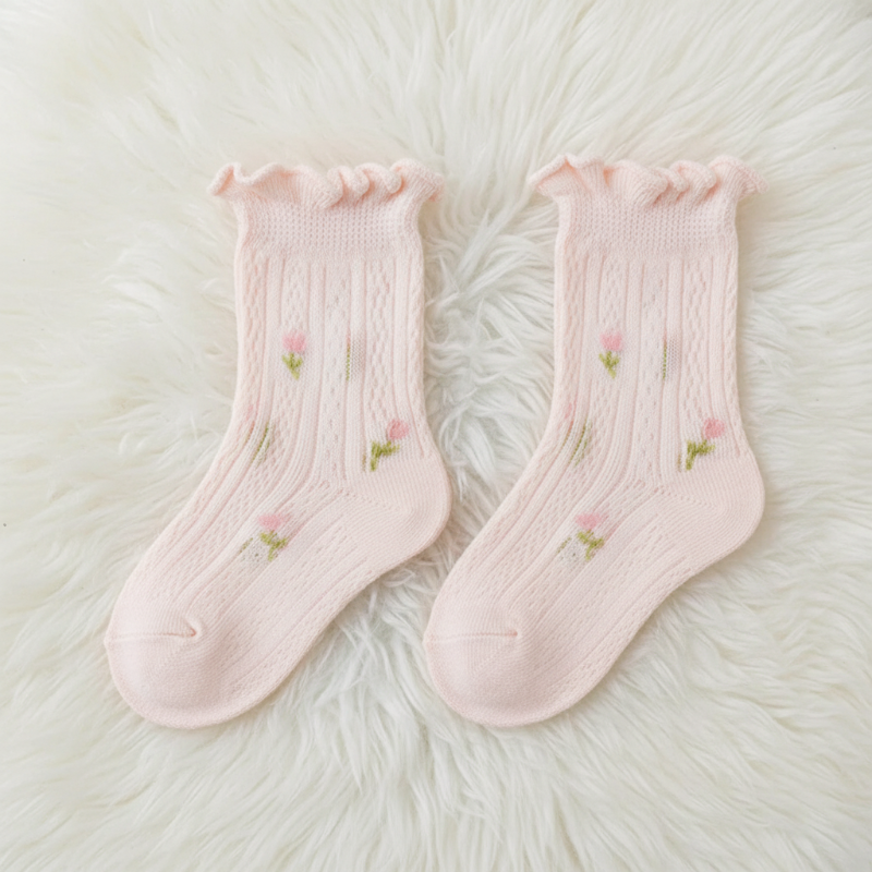 Pair of pink baby socks with floral details and ruffled cuffs on a fluffy white surface.