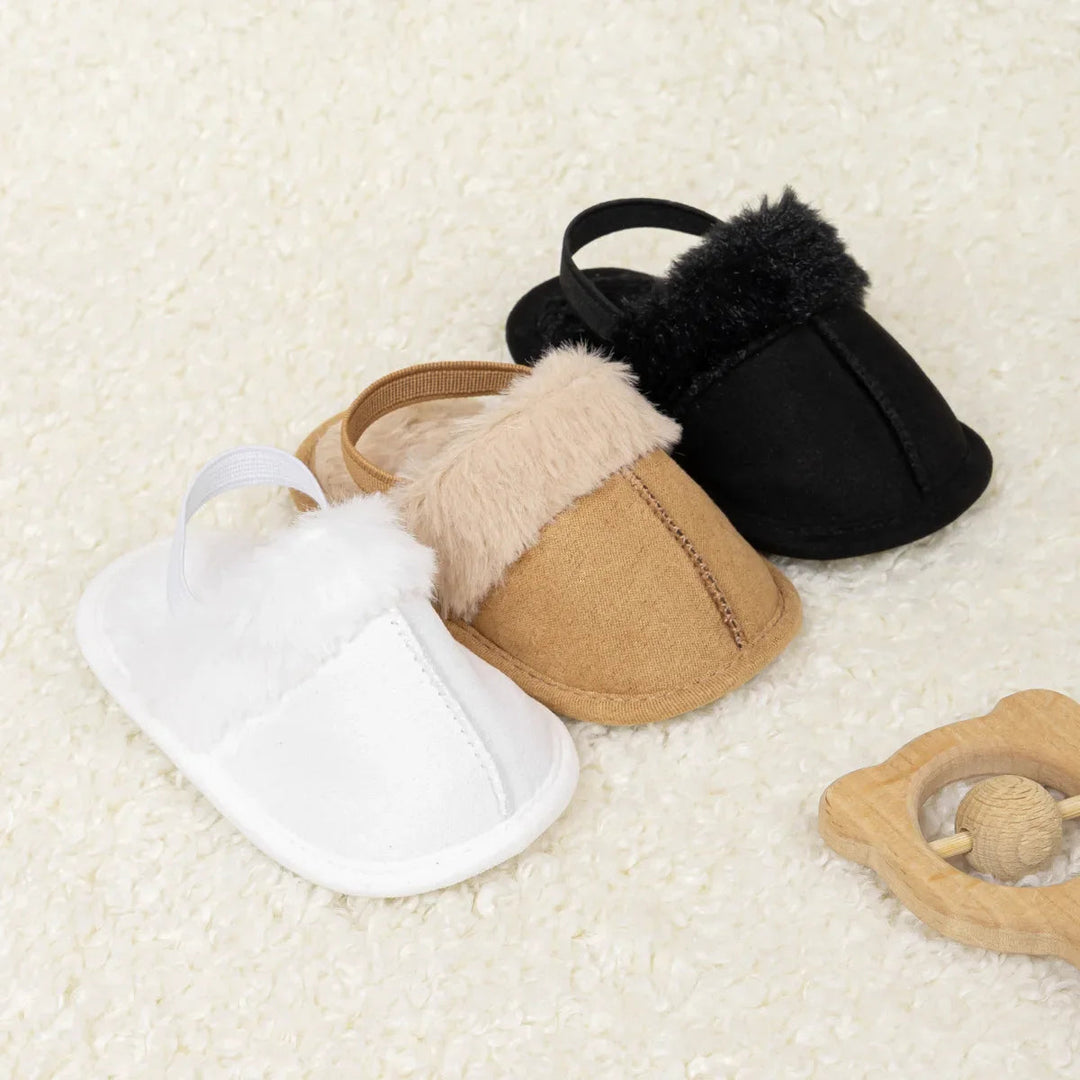 White, tan and black baby slippers arranged to show their plush openings and stitched fronts