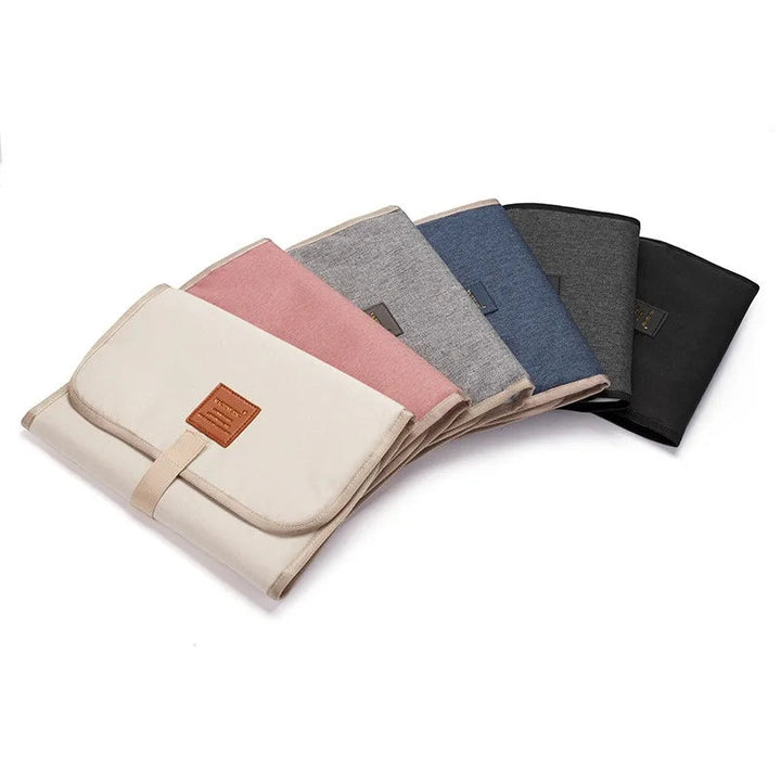 Folded baby changing mats in beige, pink, light gray, blue, dark gray and black