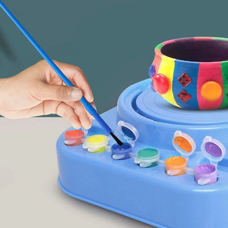 Paintbrush dipping into blue paint beside a colorful pot on the pottery wheel