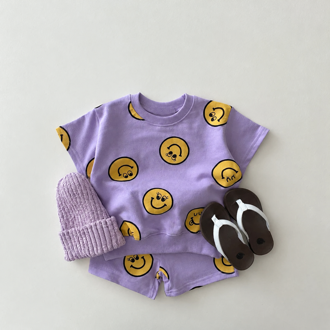 Purple smiley-print T-shirt and matching shorts styled with a purple knit hat and black sandals