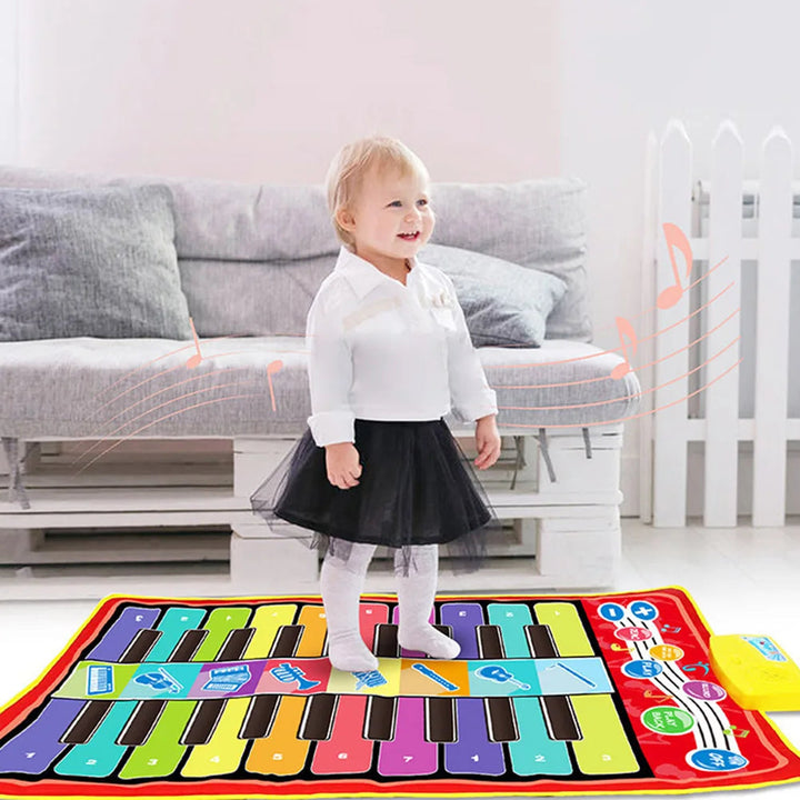 Child standing on a rainbow-key piano mat beside a gray sofa