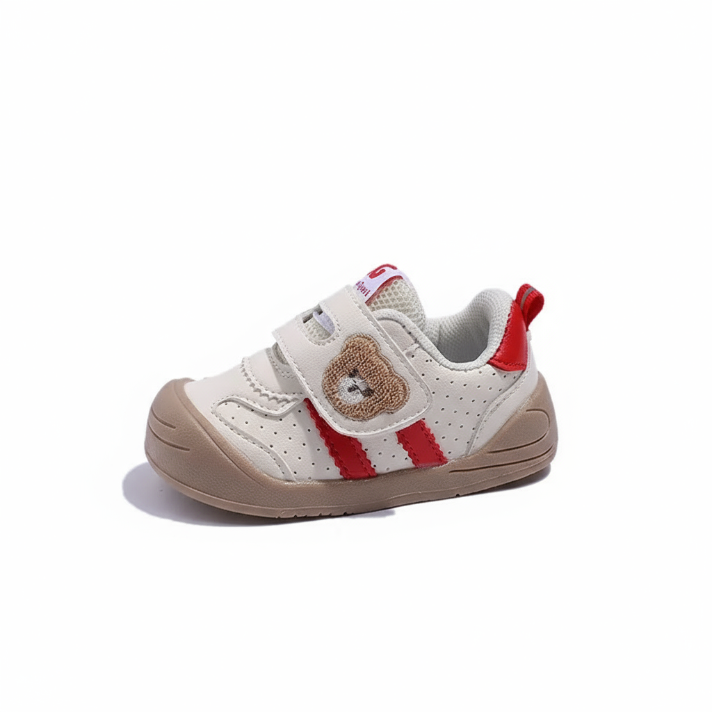 Side view of a cream sneaker with a bear strap, red side accents, and a tan sole