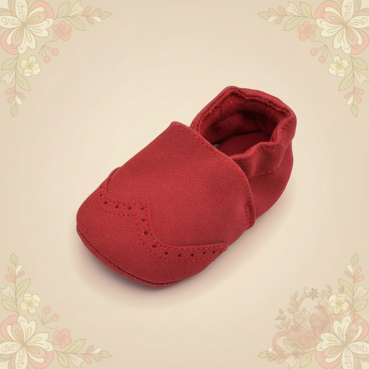 Single red baby shoe showing its rounded toe and brogue-style perforations