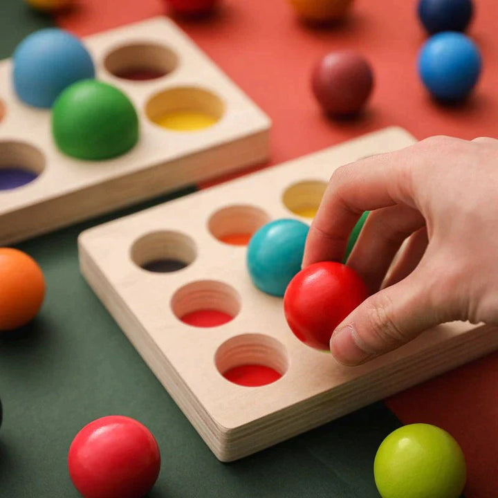 A hand places a red ball into a matching space on the wooden sorting board