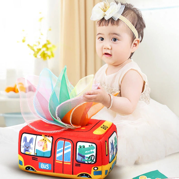 Child holding a colorful fabric tissue above a red bus tissue box