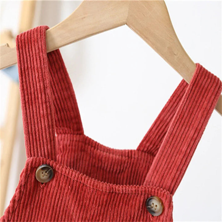 Close-up of red corduroy overall straps and front button fastenings on a wooden hanger